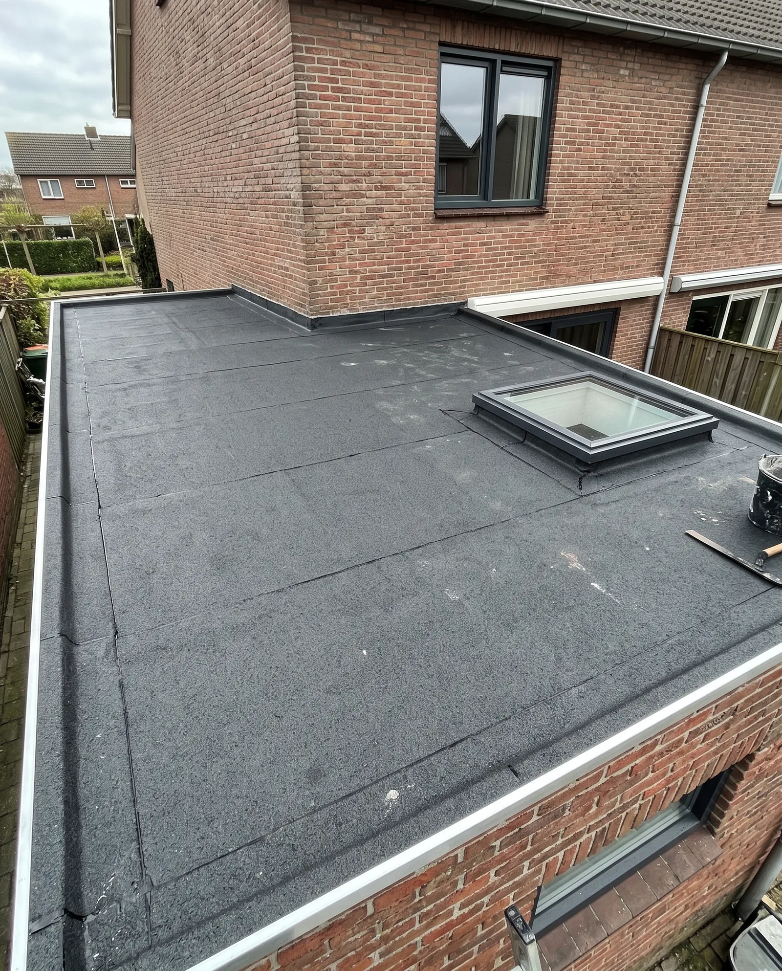 Nieuw plat dak met bitumen en strak afgewerkte daktrim, van bovenaf gezien