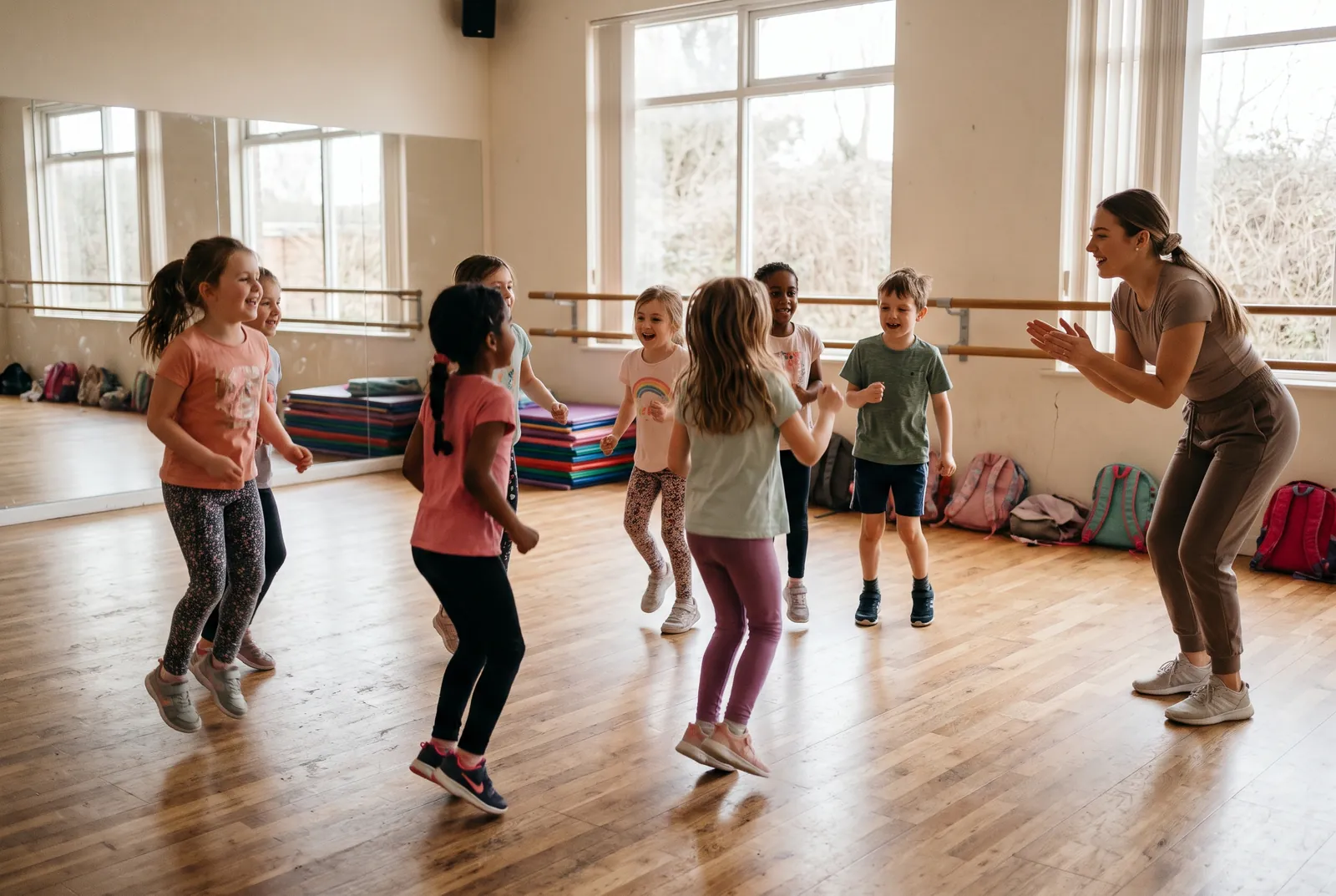 Kinderen dansen vrolijk in een lichte dansstudio terwijl de juf meeklapt