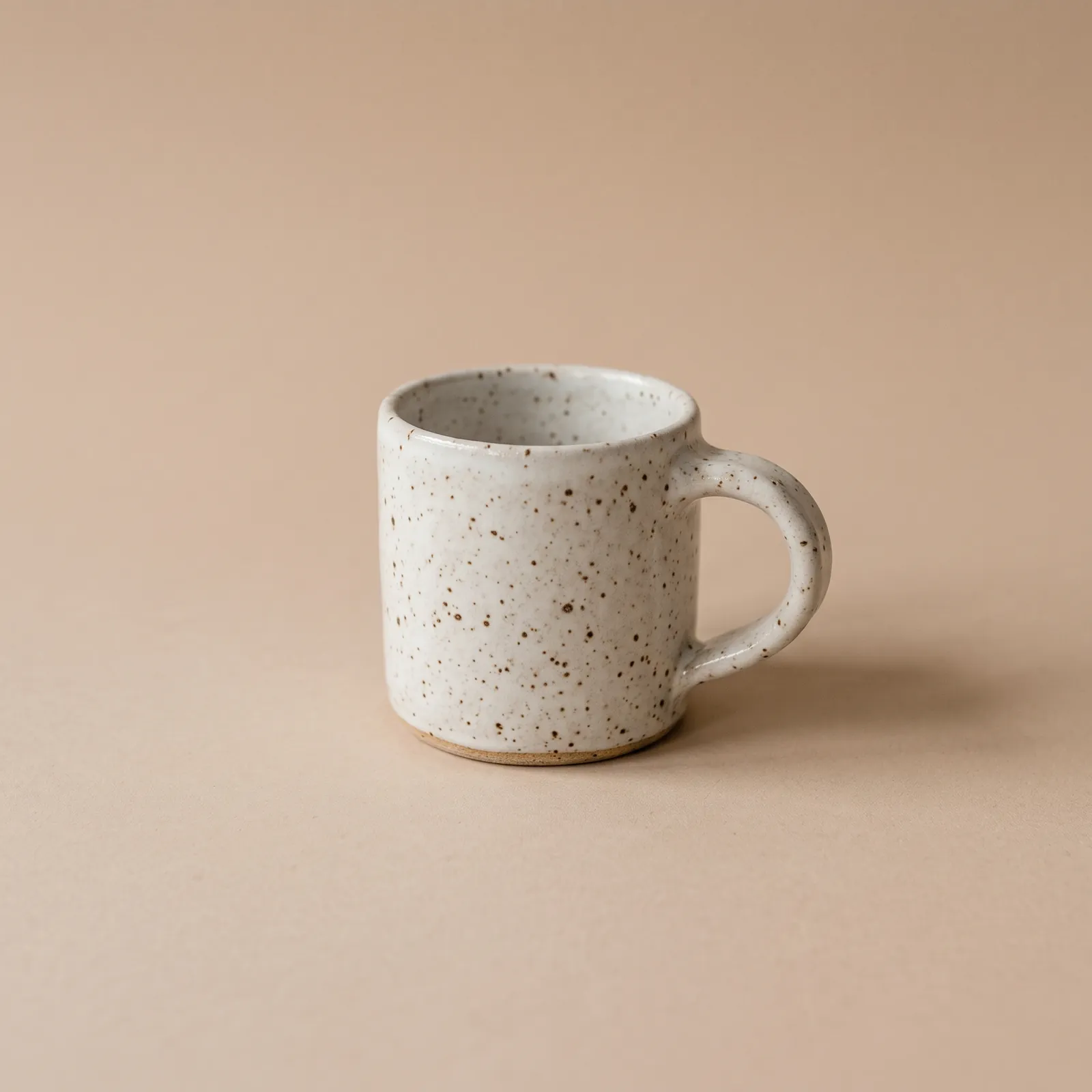 Gespikkelde handgemaakte mok op een beige achtergrond